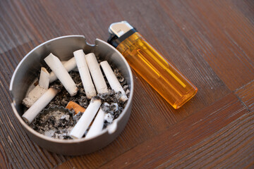 A dirty ashtray with cigarette ash,butts and lighter