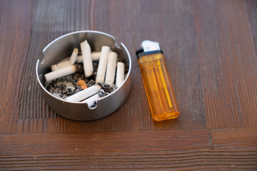 A dirty ashtray with cigarette ash,butts and lighter