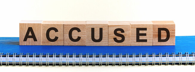 Accused - a word made of wooden blocks with black letters, a row of blocks is located on a blue Notepad. White background, front view. Accused code, promo code concept.