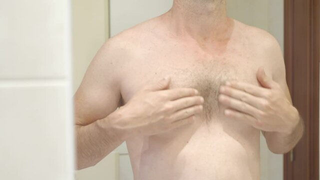 caucasian shirtless man with hair on his chest looking at himself in bathroom mirror