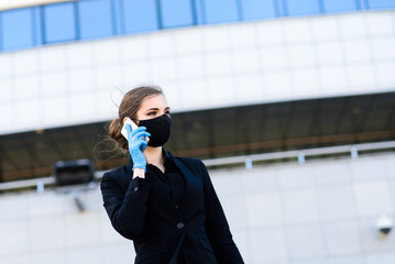 Beautiful businesswoman in a black suit in a black medical mask and gloves at the city in quarantine and isolation. Pandemic COVID-19. Selective focus