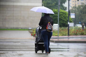 a woman with a pram crosses the street with an umbrella in the rain