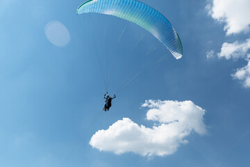 Blue Paraglider flying into the sky with clouds on a sunny day
