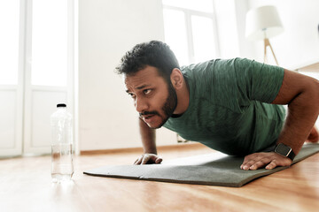 Young active man looking focused, exercising, doing push ups during morning workout at home. Sport, healthy lifestyle - obrazy, fototapety, plakaty
