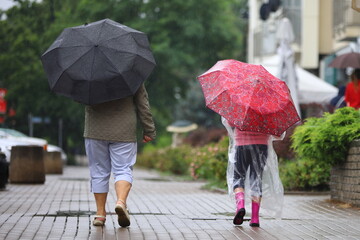 little girl mom with umbrella walks down the street in the rain
