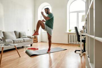 Get Fit. Full length shot of young active man watching online video training on laptop, exercising during morning workout at home. Sport, healthy lifestyle