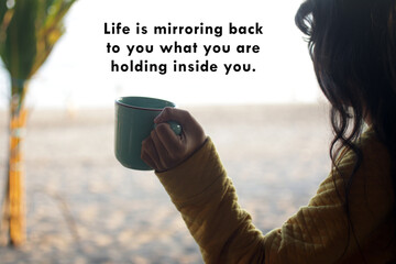 Inspirational motivational quote - Life is mirroring back to you what you are holding inside you. With young woman holding a cup of morning coffee looking at the beach view background.