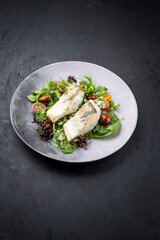 Traditionelles gebratenes Skrei Kabeljau Fisch Filet mit  italienischen Salat und Tomaten in einer Zitronen Kokos Sauce angeboten als Draufsicht in einem Modern Design Teller mit Textfreiraum