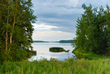 Summer landscape. In the photo, a forest lake, in the background, a forest and gray clouds.