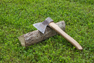 Old ax for chopping firewood and forest on a background of green grass.
