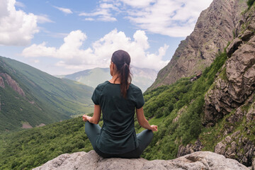 Naklejka na ściany i meble Beautiful young woman meditating on a rock in mountain