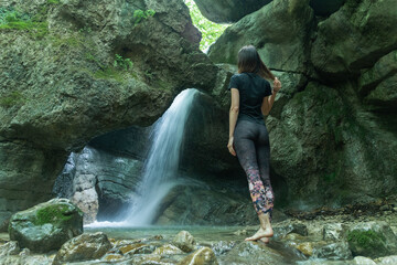 Young woman looking at splashing waterfall in rocky mountain. Caucasian Traveler standing before water stream.