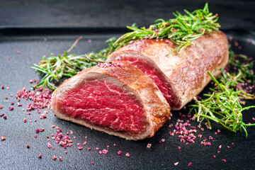 Fried dry aged beef fillet steak natural with herb and red wine salt offered as close-up on a black modern design tray