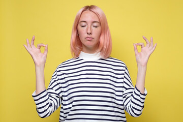 Beautiful casually dressed young woman keeping eyes closed while meditating, feeling relaxed