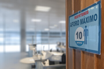 Cartel de seguridad en español en una oficina con atencion al publico. Aforo Maximo de personas. Covid 19. Seguridad