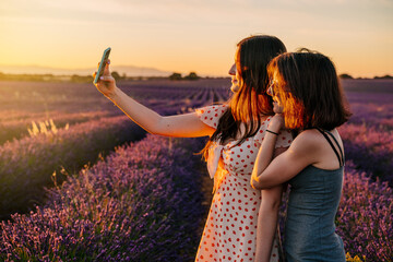 Two friends take photos with their mobile phone in a field of blooming lavenders