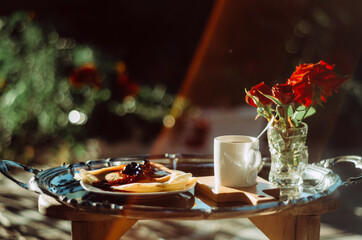 Still life shot of  breakfast tray silver platter with cup of coffee, roses and pancakes bathed in golden light with lens flare