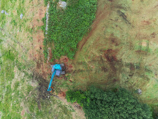 Obraz premium Aerial view on a blue excavator working ina blue field by a stone fence. Top down view. Construction and renovation concept.