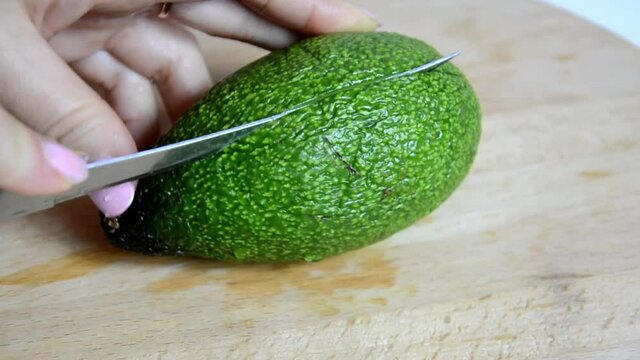 Closeup of female hands cooking with avocado at table in home kitchen. Getting the seed out and cut slices