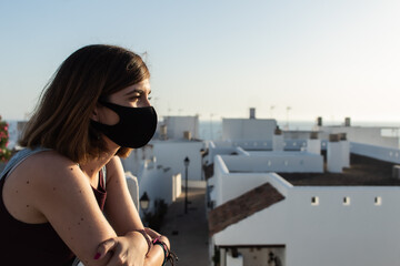 Fototapeta na wymiar Attractive young female wearing a face mask and witnessing the sunset from a viewpoint located in a small village in Cadiz, Spain