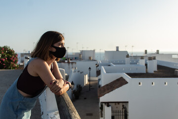 Fototapeta na wymiar Attractive young female wearing a face mask and witnessing the sunset from a viewpoint located in a small village in Cadiz, Spain