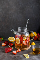 Fruit tea in a large transparent teapot. Warm lemonade with fruits and berries. Dark photo. Minimalism. Beautiful dishes.