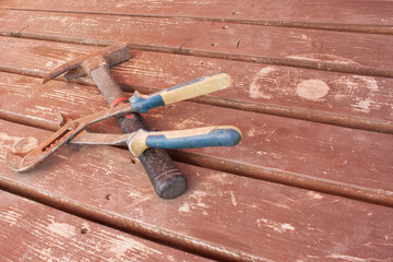 Large rusty pliers with plastic handles and a hammer against a background of brown old wooden...