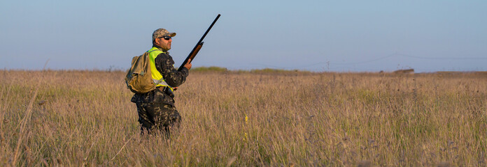 Silhouette of a hunter with a gun in the reeds against the sun, an ambush for ducks with dogs