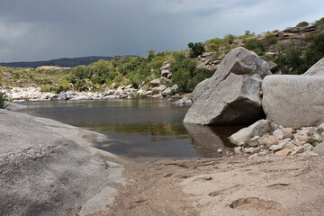 View form the sand shore of the river flowing along the rocky valley and mountain forest. 