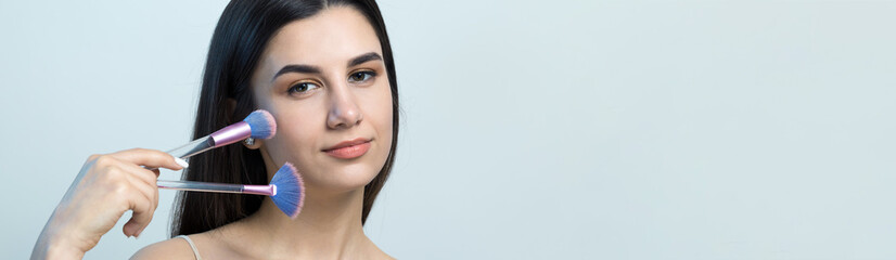 Close-up of a young girl in a light top on a white background making a facial make-up. A pretty...