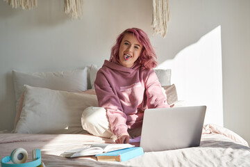 Cool hipster teen girl school gen z college student with pink hair wears hoodie sits on bed with...