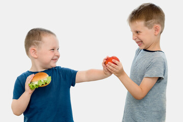 Two boys on a white background, one with a hamburger, the second offers him fruit.Concept-the older brother insistently suggests that the younger one should change junk food for a healthy lifestyle.