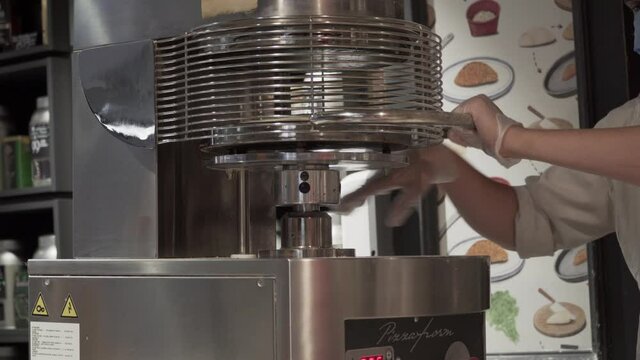 The hands of a chef in a fast food restaurant uses a pizza press tool to reshape the dough from a ball to flat. Press Flow Chart pizza, pizza oven. Unit, tool. Press Machine To Make Pizza.