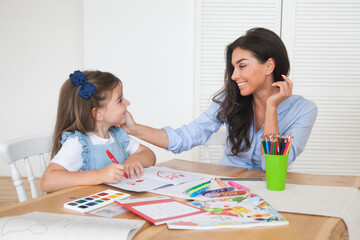 Smiling mother and daughter preparing for lessons and draws at the table with pencils and paints. Parent and pupil of preschool. First day of fall autumn. Girl from elementary class, back to school