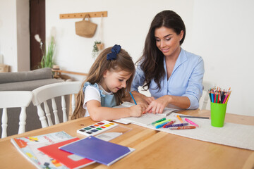 Smiling mother and daughter preparing for lessons and draws at the table with pencils and paints. Parent and pupil of preschool. First day of fall autumn. Girl from elementary class, back to school