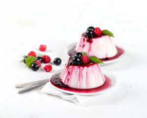 Panna cotta cream with berry sauce and fresh raspberries and black currants on a white background