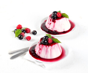 Panna cotta cream with berry sauce and fresh raspberries and black currants on a white background