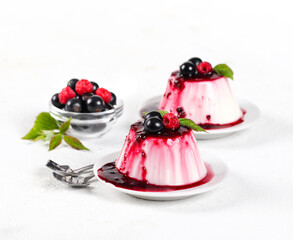Panna cotta cream with berry sauce and fresh raspberries and black currants on a white background