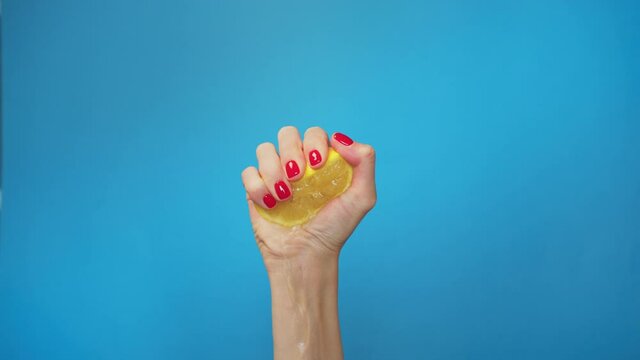 Slow Motion squeeze juice from lemon, close up woman hand squeezes half yellow lemon on blue background. Exhausted.