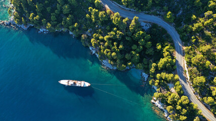 Aerial top down photo of snake road covered in pine trees leading to famous and picturesque small...