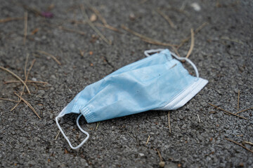 Medical protective mask thrown on the ground on asphalt in day close up - Waste Covid-19...