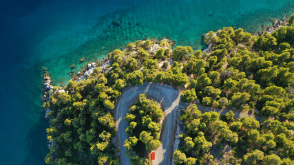 Aerial top down photo of snake road covered in pine trees leading to famous and picturesque small...
