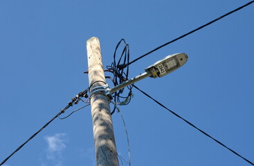 Many electric wires on concrete street pole with internet or cell phone communication box on blue...