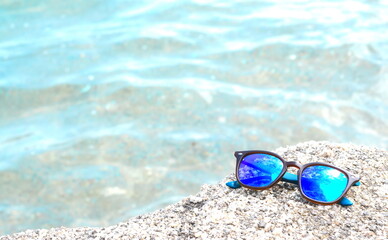 Fototapeta na wymiar Close up of sand and sunglasses with blurred sea background.