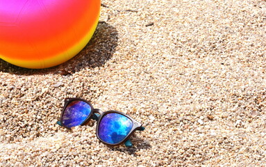 Fototapeta na wymiar Close up of sand and sunglasses with blurred sea background.