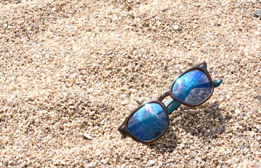 Close up of sand and sunglasses with blurred sea background.