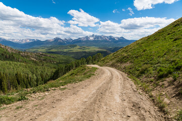 Four wheel drive road above a landscape of snow-capped mountains and aspen groves in the Colorado...