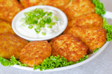 Draniki, hash browns or potato pancakes served with fresh cream and green onions close-up