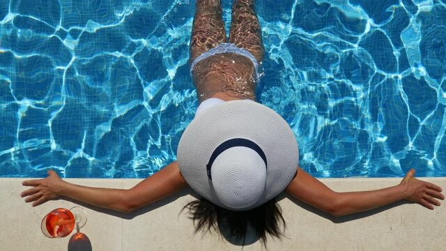 Sexy woman sitting at poolside and drinking cocktail, top view