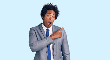 Handsome african american man with afro hair wearing business jacket surprised pointing with finger to the side, open mouth amazed expression.